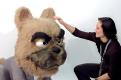 Custom animatronic bulldog mascot in business suit—furry head with grumpy expression, woman interacting at trade show booth