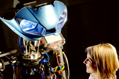 big animatronic robot shaking hands with a girl bright blue lights and exposed electronics and mechanical gear and electric actuators