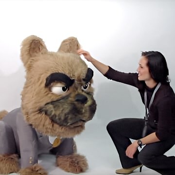 Custom animatronic bulldog mascot in business suit—furry head with grumpy expression, woman interacting at trade show booth