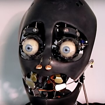 Custom animatronic robotic head prototype—matte black shell, exposed blue-eyed mechanisms, brass gears and wiring in open jaw.