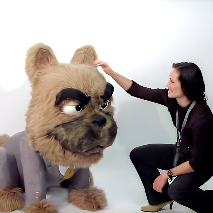 Custom animatronic bulldog mascot in business suit—furry head with grumpy expression, woman interacting at trade show booth