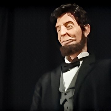 A full-body, life-scale animatronic replica of Abraham Lincoln, complete with authentic 19th-century attire, detailed silicone skin, bushy beard, parted dark hair, and realistic facial movements—engineered to recite the Gettysburg Address with programmed gestures and voice, blending robotics and historical education