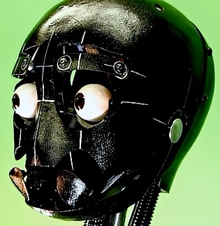 A close-up of a sleek black carbon fiber composite robot head, featuring eerily realistic human eyes set into a grid-patterned faceplate, metallic screws, hoses, and a hinged mouth mechanism—mounted on a green studio background, blending human anatomy with advanced robotics