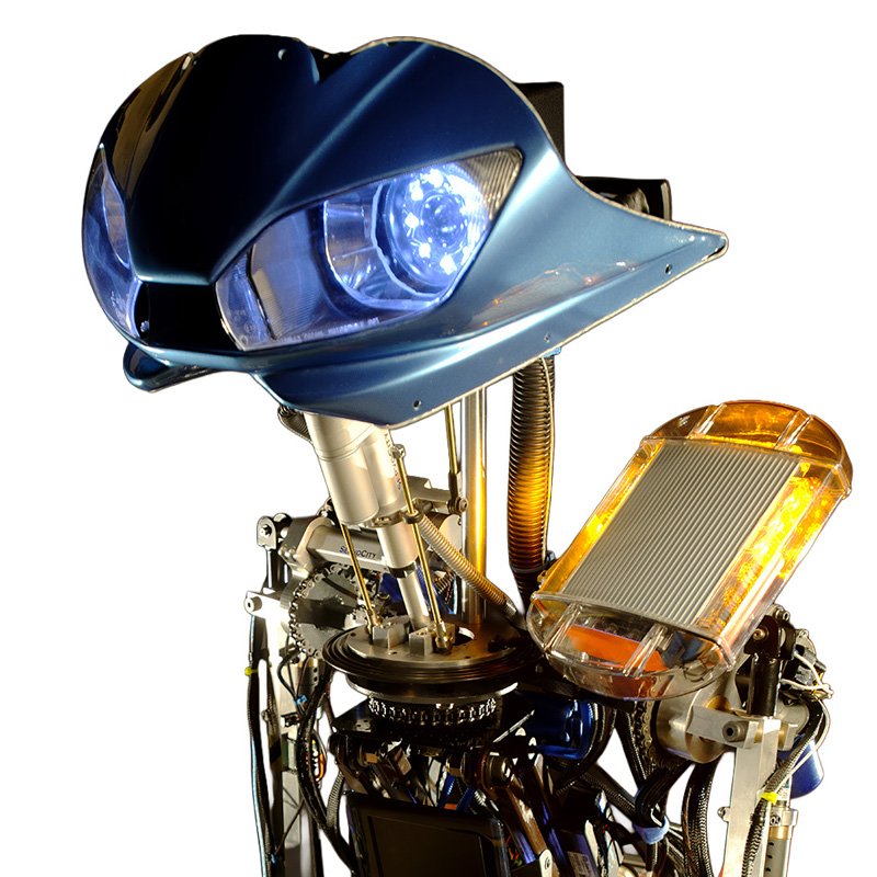 Giant animatronic robot with bright blue LED eyes, exposed CNC aluminum mechanisms, and yellow safety beacon